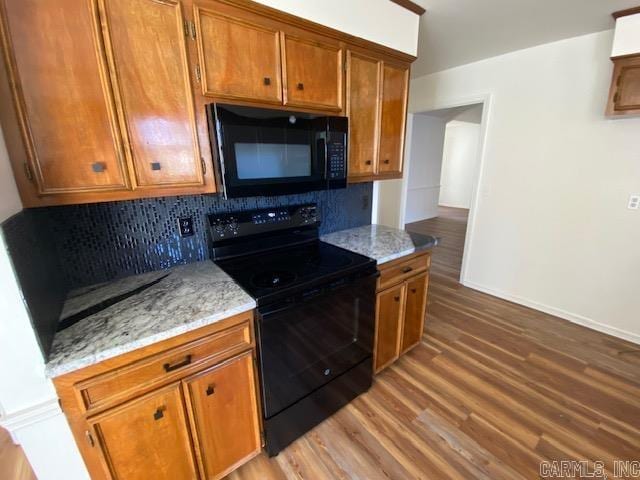 kitchen with tasteful backsplash, wood-type flooring, light stone countertops, and black appliances