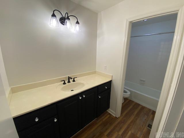 full bathroom with hardwood / wood-style flooring, vanity, shower / bath combination, and toilet