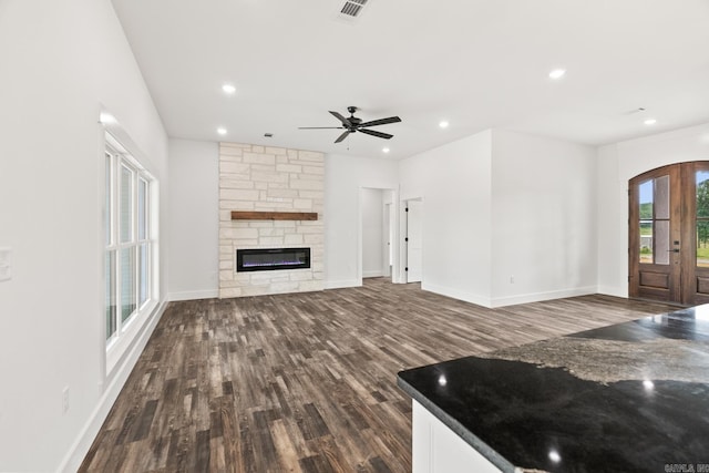 unfurnished living room featuring a stone fireplace, ceiling fan, french doors, and dark wood-type flooring