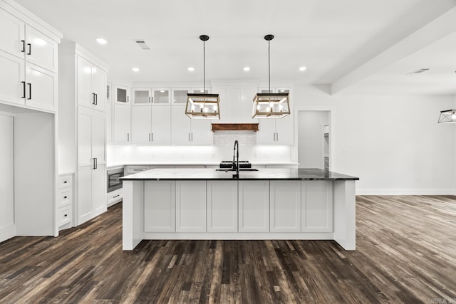 kitchen with white cabinets, dark hardwood / wood-style flooring, decorative light fixtures, and an island with sink