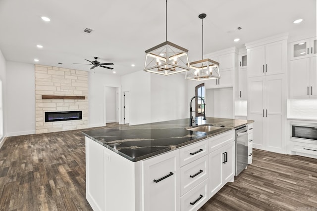 kitchen with white cabinetry, sink, a stone fireplace, pendant lighting, and a center island with sink