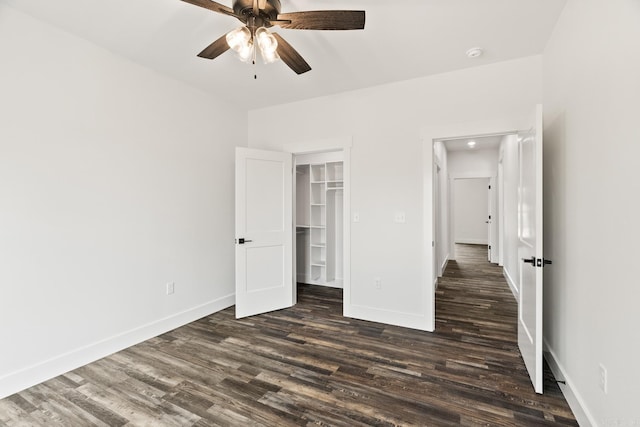 unfurnished bedroom with a closet, ceiling fan, dark hardwood / wood-style flooring, and a walk in closet