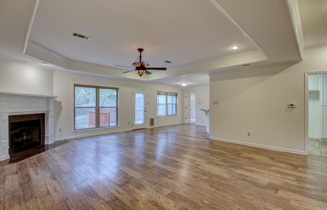 unfurnished living room featuring a raised ceiling, ceiling fan, crown molding, and light wood-type flooring