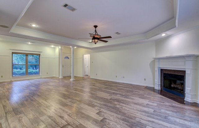 unfurnished living room with ceiling fan, a raised ceiling, decorative columns, wood-type flooring, and ornamental molding