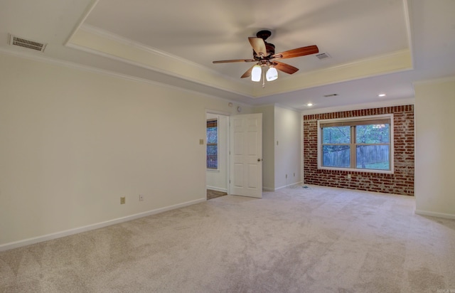 carpeted empty room featuring ceiling fan, ornamental molding, brick wall, and a tray ceiling