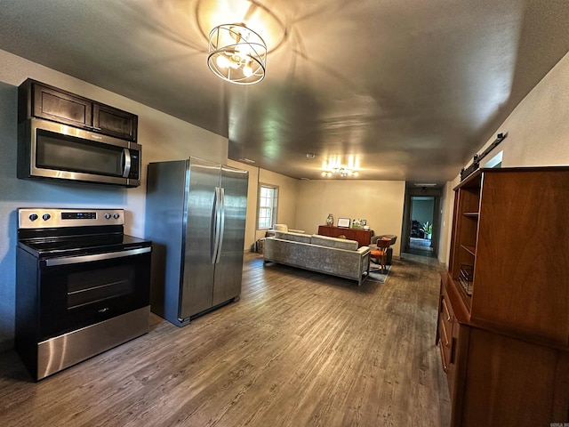 kitchen featuring dark brown cabinets, stainless steel appliances, a barn door, an inviting chandelier, and dark hardwood / wood-style floors