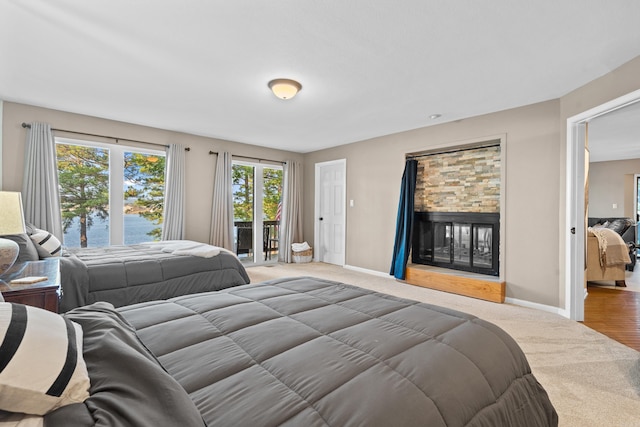 bedroom featuring access to outside, a stone fireplace, a water view, and carpet