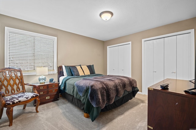 bedroom featuring light colored carpet and two closets