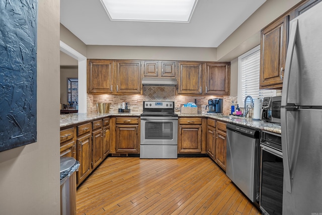 kitchen featuring light stone countertops, sink, light hardwood / wood-style flooring, decorative backsplash, and appliances with stainless steel finishes