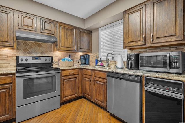 kitchen featuring sink, light stone countertops, light wood-type flooring, appliances with stainless steel finishes, and tasteful backsplash