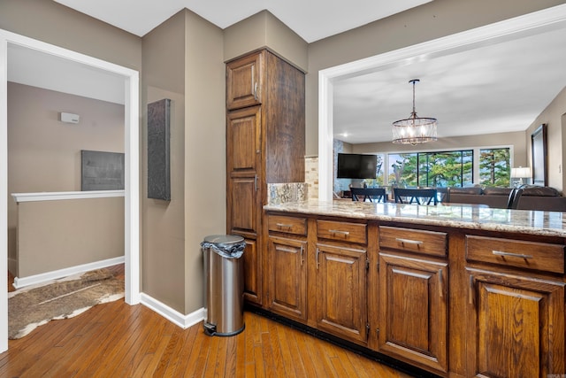 kitchen featuring light stone countertops, decorative light fixtures, an inviting chandelier, and light hardwood / wood-style flooring