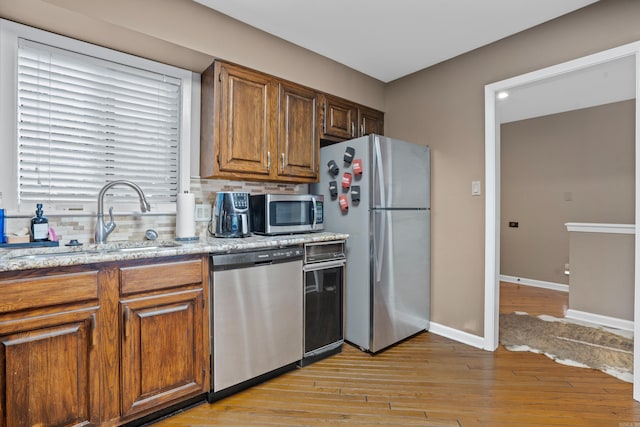 kitchen with light stone countertops, sink, tasteful backsplash, light hardwood / wood-style flooring, and appliances with stainless steel finishes