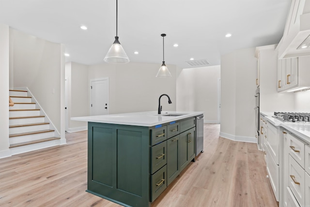 kitchen featuring sink, decorative light fixtures, a kitchen island with sink, white cabinets, and light wood-type flooring