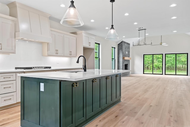 kitchen featuring ceiling fan, sink, white cabinetry, hanging light fixtures, and an island with sink