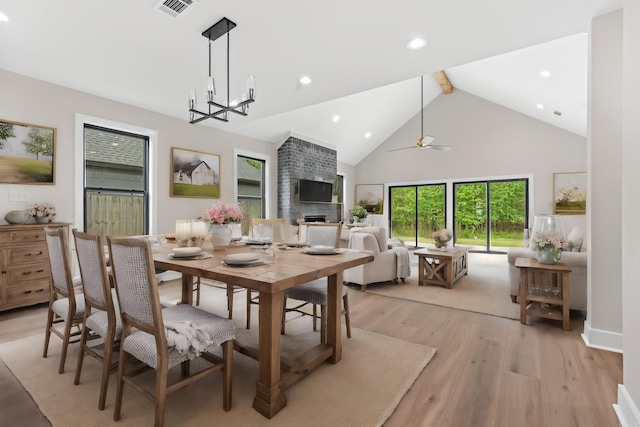 dining space with ceiling fan with notable chandelier, high vaulted ceiling, and light hardwood / wood-style flooring