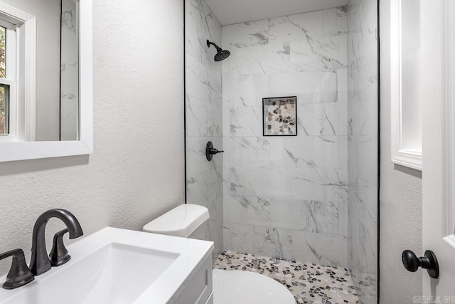 bathroom with tiled shower, vanity, and toilet