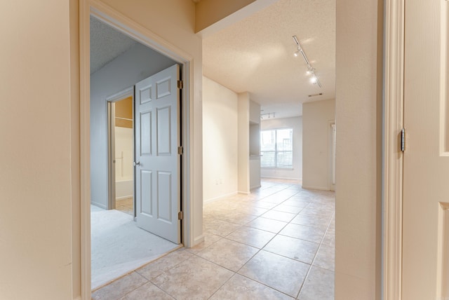 corridor with rail lighting, light tile patterned flooring, and a textured ceiling