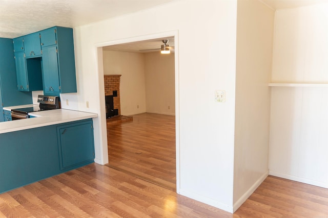 kitchen with a fireplace, light hardwood / wood-style floors, blue cabinets, and stainless steel electric stove