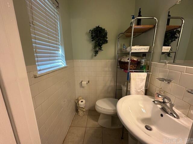 bathroom featuring tile patterned floors, toilet, sink, and tile walls