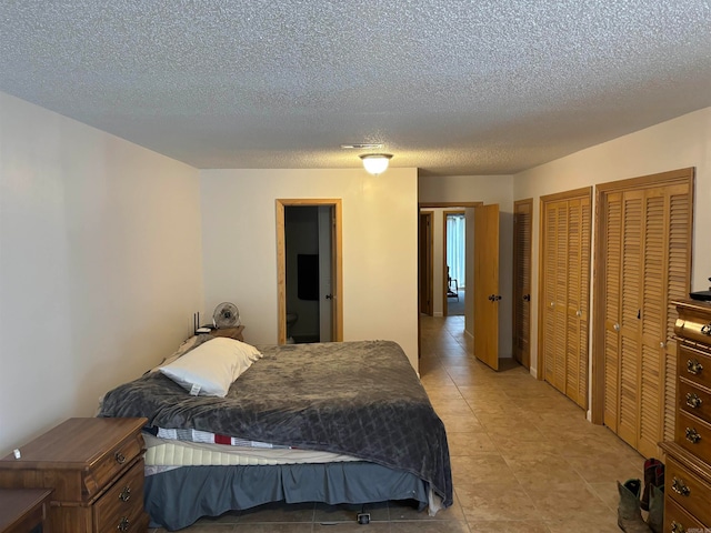 bedroom featuring two closets, light tile patterned flooring, and a textured ceiling