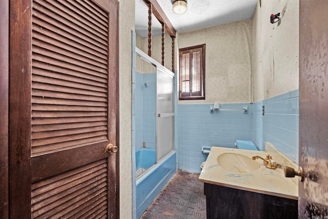 bathroom with combined bath / shower with glass door, vanity, a textured ceiling, and tile walls