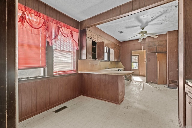 kitchen featuring plenty of natural light, kitchen peninsula, a textured ceiling, and wooden walls