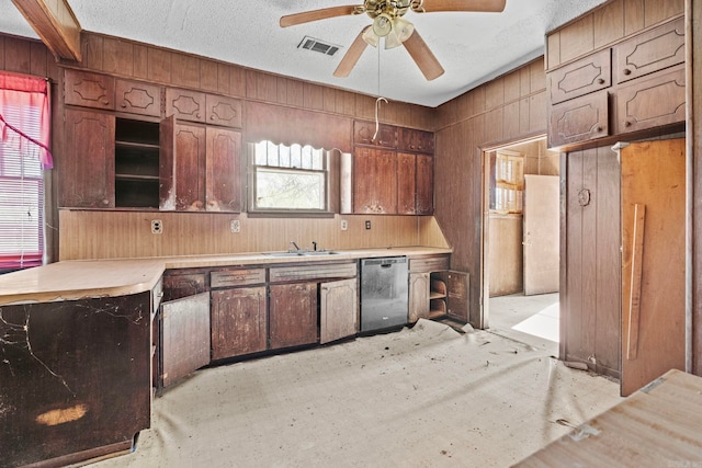 kitchen featuring stainless steel dishwasher, a textured ceiling, ceiling fan, sink, and wood walls