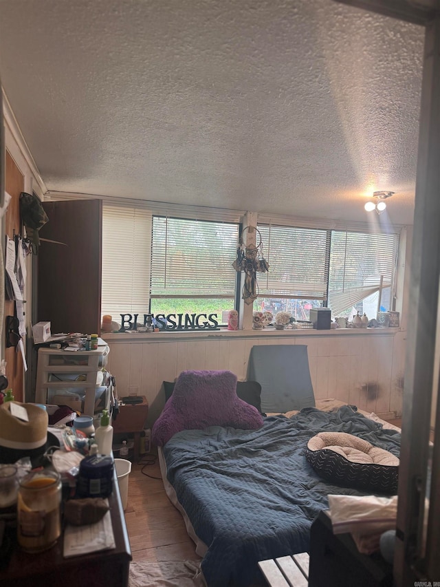 bedroom with wood-type flooring, a textured ceiling, multiple windows, and wood walls