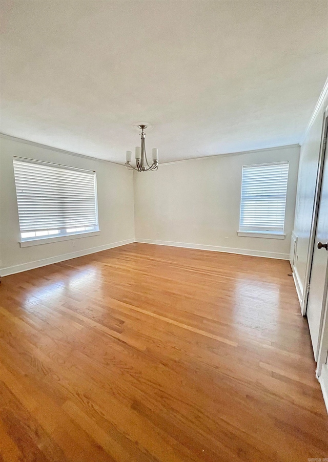 empty room featuring a healthy amount of sunlight, ornamental molding, light hardwood / wood-style flooring, and a chandelier