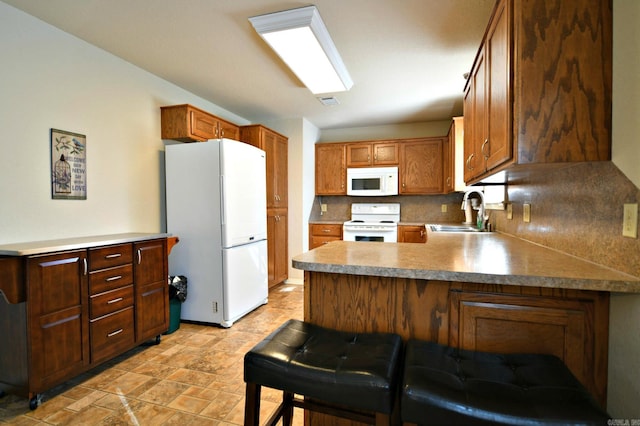 kitchen with white appliances, a kitchen breakfast bar, sink, tasteful backsplash, and kitchen peninsula