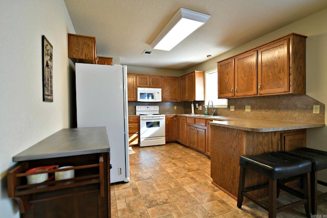 kitchen with kitchen peninsula, backsplash, a breakfast bar, white appliances, and sink