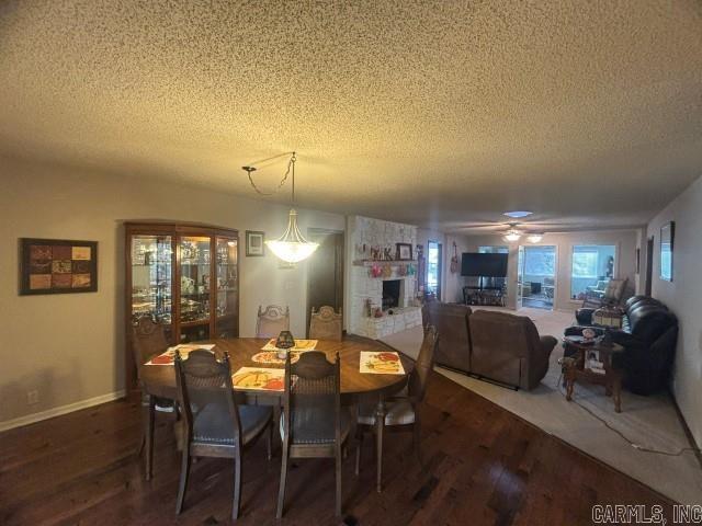 dining space with a textured ceiling, dark hardwood / wood-style flooring, a stone fireplace, and ceiling fan