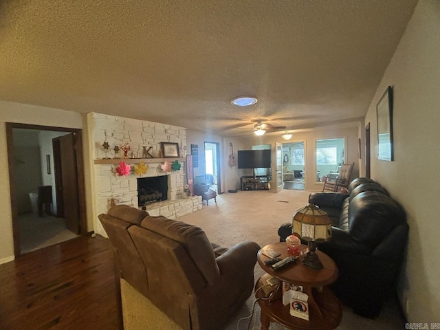 living room featuring a fireplace, ceiling fan, a textured ceiling, and a wealth of natural light