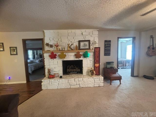 living room with carpet, a textured ceiling, a stone fireplace, and ceiling fan