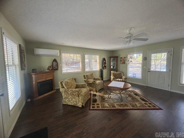 living room featuring a wall mounted air conditioner, a textured ceiling, ceiling fan, and dark wood-type flooring