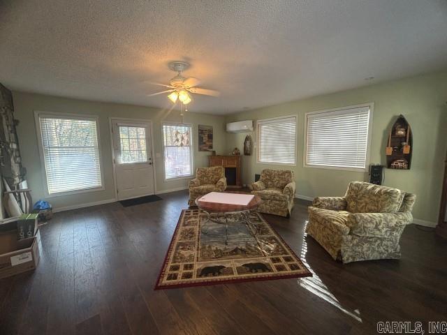 living room with ceiling fan, dark hardwood / wood-style flooring, an AC wall unit, and a textured ceiling