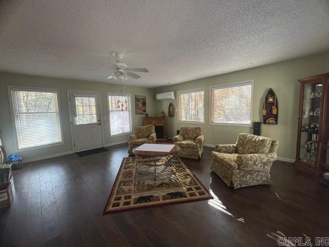 living room with a healthy amount of sunlight, dark hardwood / wood-style flooring, a textured ceiling, and a wall unit AC