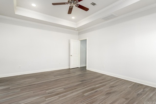 empty room with a raised ceiling, crown molding, ceiling fan, and dark wood-type flooring