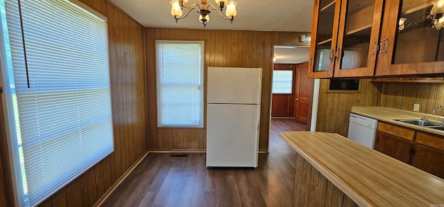 kitchen with sink, dark hardwood / wood-style flooring, a notable chandelier, wood walls, and white appliances