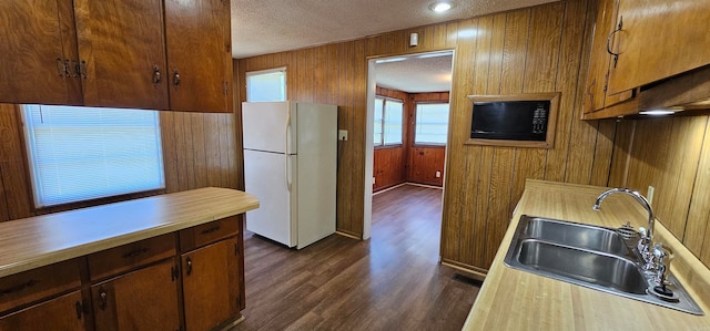 kitchen featuring sink, dark wood-type flooring, white refrigerator, wood walls, and a textured ceiling