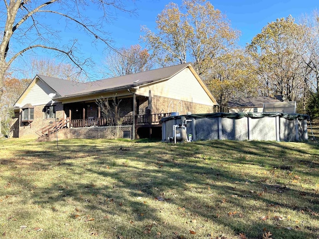 rear view of house featuring a covered pool, a lawn, and brick siding