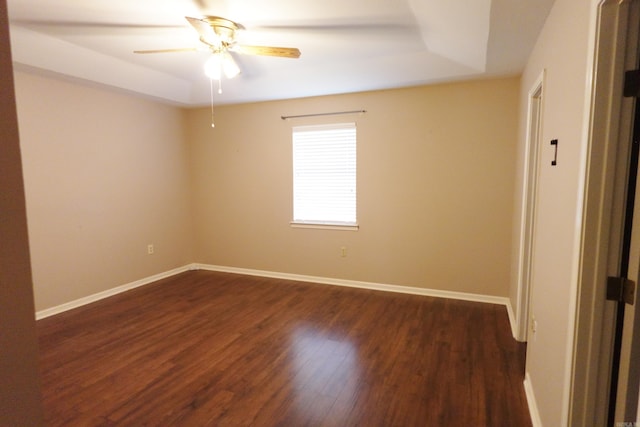 unfurnished room with a raised ceiling, ceiling fan, and dark hardwood / wood-style flooring