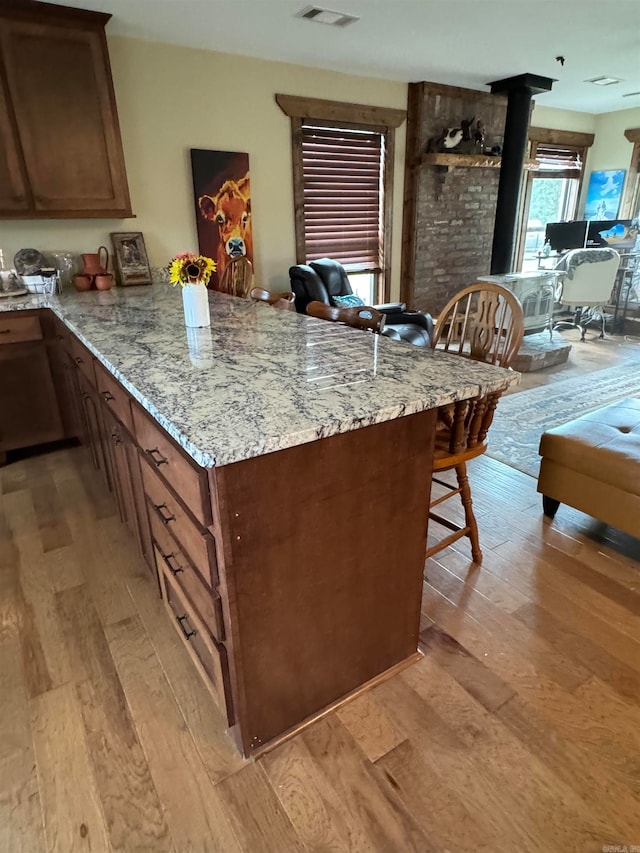 kitchen featuring a wood stove, light stone countertops, light hardwood / wood-style floors, a kitchen bar, and kitchen peninsula