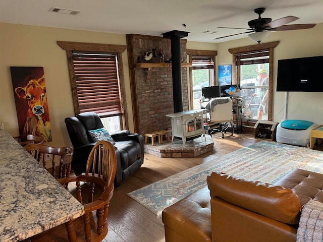 living room featuring ceiling fan, wood-type flooring, and a wood stove