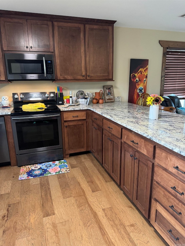 kitchen with kitchen peninsula, light stone countertops, stainless steel appliances, and light hardwood / wood-style floors