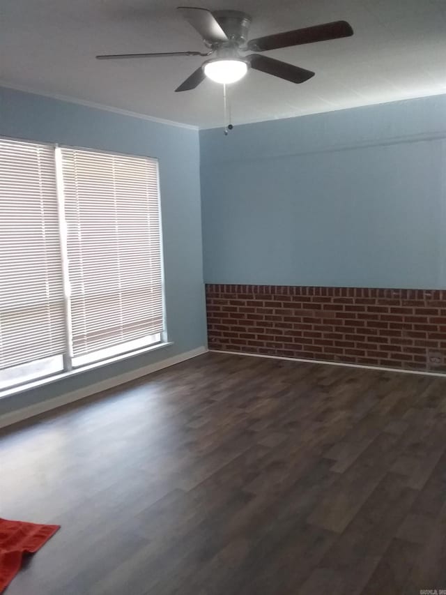 unfurnished room featuring dark hardwood / wood-style floors, ceiling fan, ornamental molding, and brick wall