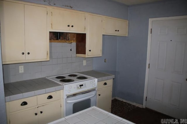 kitchen featuring white range with electric stovetop, tile countertops, decorative backsplash, and cream cabinets