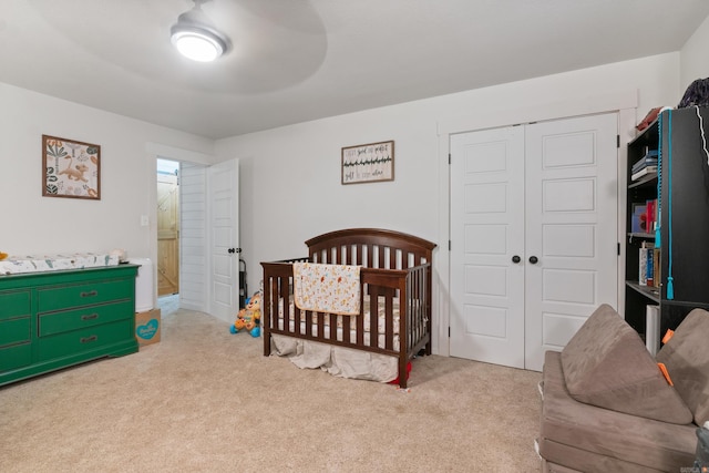 bedroom featuring a crib, light carpet, a closet, and ceiling fan