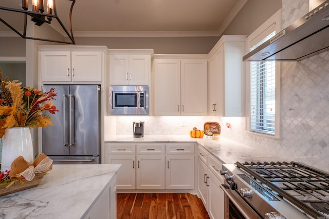 kitchen with backsplash, white cabinets, wall chimney exhaust hood, ornamental molding, and premium appliances