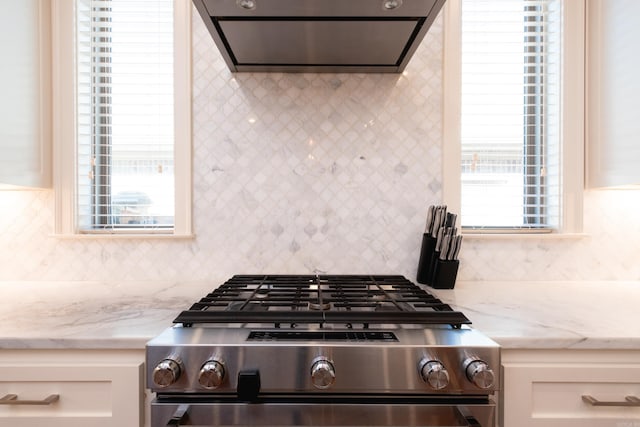 kitchen featuring light stone countertops, stainless steel range, white cabinetry, extractor fan, and decorative backsplash